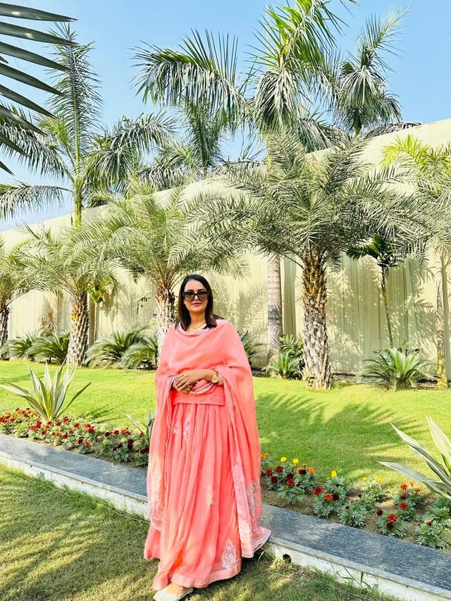 Woman in sunglasses wearing a coral-peach lehenga set with a sheer dupatta in a palm garden